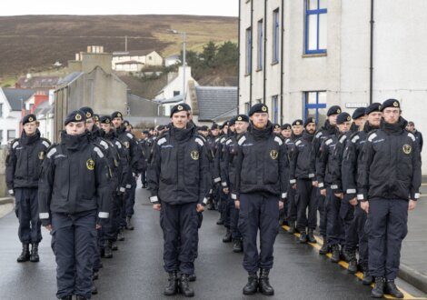 Uniformed personnel marching in formation through a street.