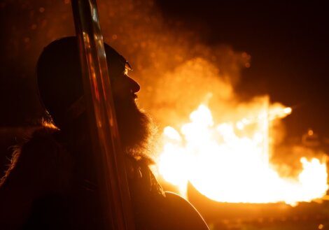 A person silhouetted against the glow of a large fire at night.