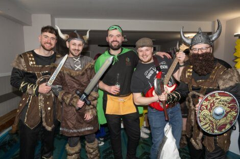 Group of men in various costume attire posing for a photo at an event.