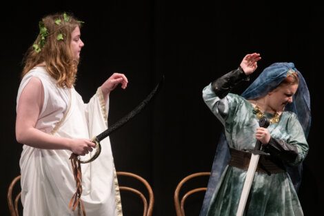 Two actors in ancient roman costumes perform a dramatic scene on stage.