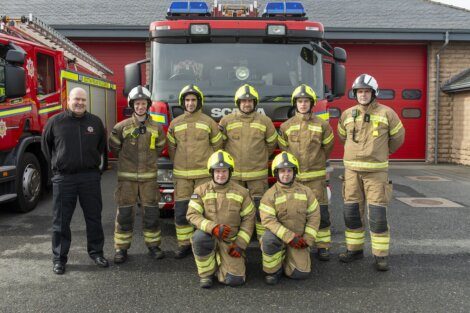 Group of firefighters standing in front of a fire truck at the station.