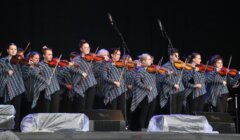 Group of violinists in matching outfits performing on stage.