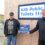 Two men standing beside a sign that reads "aith public toilets," one of them holding a small award that says "coastal aquaculture scotland.