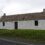 A traditional whitewashed stone cottage with a thatched roof, two chimneys, and a single door, set against a cloudy sky.