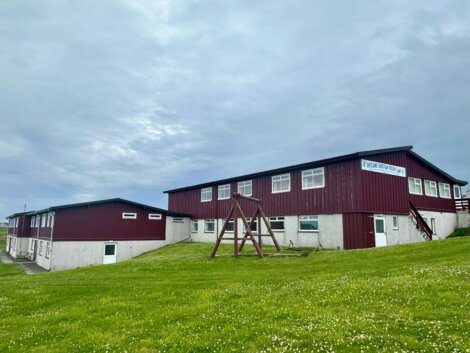 Two connected red and white buildings under a cloudy sky with a wooden swing set in the foreground, situated on a grassy area.