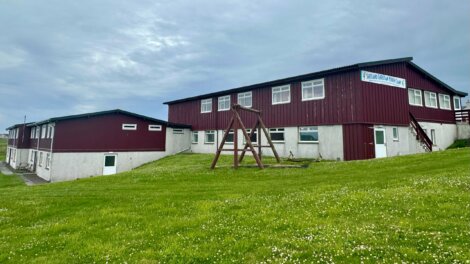 Two connected red and white buildings under a cloudy sky with a wooden swing set in the foreground, situated on a grassy area.