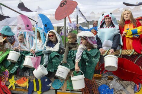Group of people in ocean-themed costumes holding buckets stand on a decorated float.