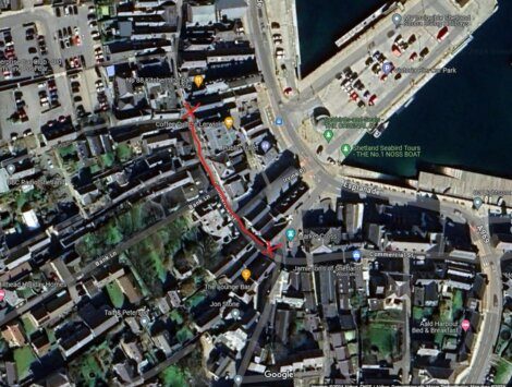 A satellite view of a town showing streets and buildings. A red line indicates a specific path or route through the area.