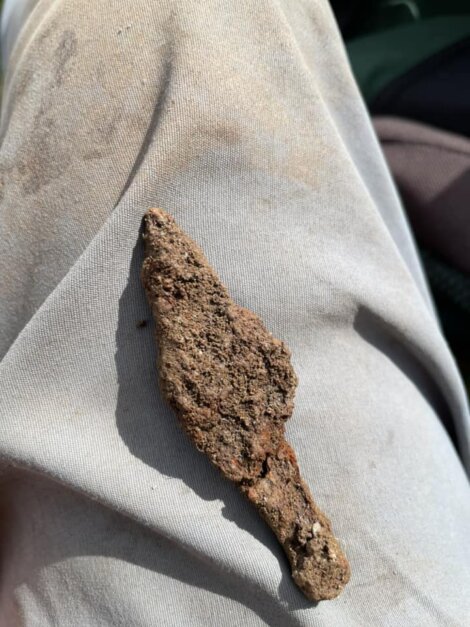A rusty, irregularly shaped metal object is seen resting on a person's light-colored clothing.