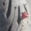 A close-up image of a tire with a sharp metal piece embedded in the tread, causing visible damage. The tire has a textured surface, and the background shows a paved road.