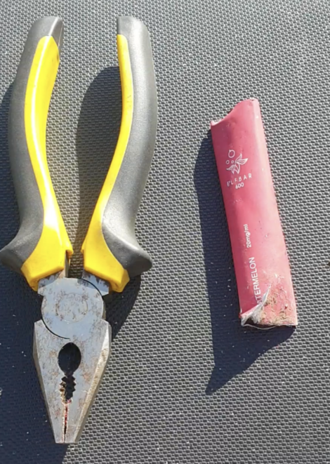 A pair of yellow-handled pliers is placed next to a section of red electrical insulation, labeled "FLEXRAD 600." Both items are on a dark textured surface.