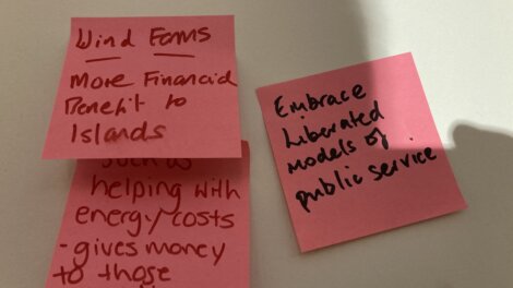 Three sticky notes with handwritten ideas: "Wind farms," "More financial benefit to islands," "Embrace liberated models of public service," and notes about helping with energy costs.