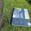 An informational sign detailing local attractions and history lies on the grass beside a paved path.