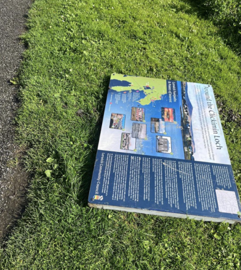 An informational sign detailing local attractions and history lies on the grass beside a paved path.