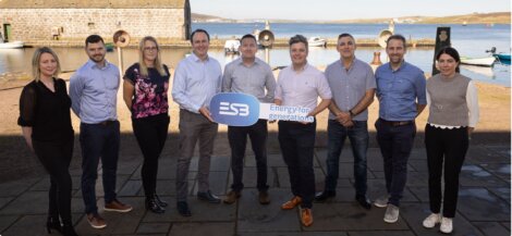 A group of nine people are standing outdoors near a waterfront, holding signs with the ESB logo and the text "Energy for generations." Buildings and boats are visible in the background.