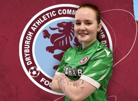 A soccer player stands confidently with arms crossed in front of a Dryburgh Athletic Community Club emblem.