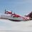 A Logan Air aircraft with tartan tail design is mid-flight against a partly cloudy sky. The plane's propellers are in motion.