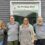Four people standing in front of a grey building with a sign that reads "Da Potting Shed." They all wear grey shirts with matching logos.