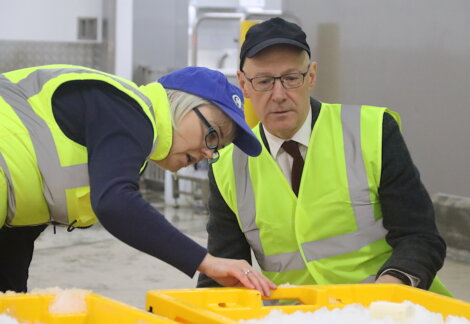 Two people wearing high-visibility vests and caps examine bins filled with ice cubes, inside an industrial setting.
