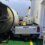 A white pickup truck with the license plate NL20 GNZ is damaged and crushed between a ferry wall and a large cylindrical object.