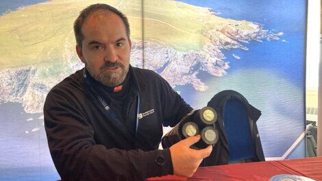 Man holding an item with three circular components, seated in front of a large aerial map backdrop.