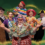 A group of six individuals in colorful costumes pose cheerfully in front of a green background with glittery accents. The text reads "Open Door Drama's Babes in the Wood.