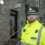 A police officer in a bright yellow uniform stands outside a stone police station building.