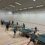 People playing table tennis in a large indoor room with multiple tables.