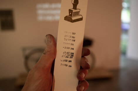 A hand holds a long piece of paper with several stamped dates, displaying a row of numbers and a stamp design at the top.