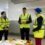 Three people in high-visibility vests and hard hats stand in a chilled warehouse, discussing near bins of ice.