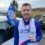 A man smiling, wearing a Mind Scotland bib, holding a medal with the number "1" on it. There's a Mind Scotland flag attached to a nearby car in the background.