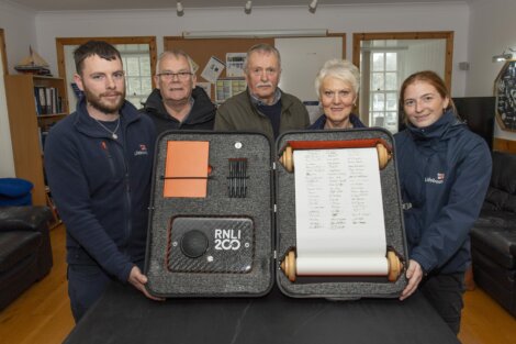 Five people holding an RNLI 200th anniversary display case with tools and a scroll.