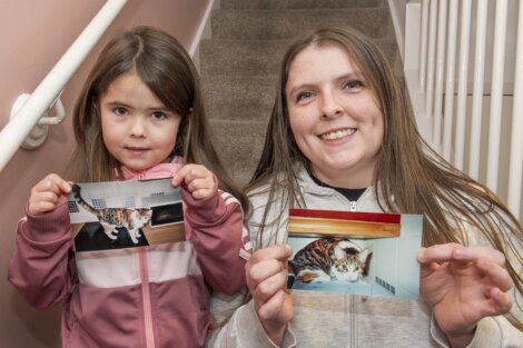 A woman and a young girl stand on stairs, each holding a photo of a cat.
