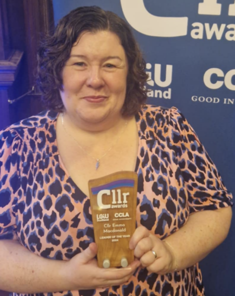 A person holding a wooden plaque in front of a blue banner with "Cllr awards" text.