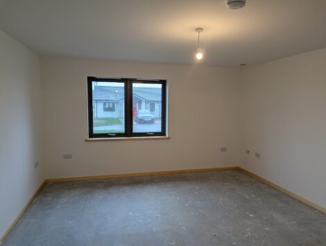Empty room with unpainted concrete floor, white walls, a window with a view of houses, and a ceiling light fixture.