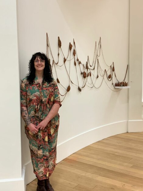 A person stands in a gallery next to an abstract wall installation made of strings and organic shapes.