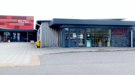 Exterior of Mid Yell Junior High and Nursery, featuring modern architecture with a combination of wood, stone, and large glass windows.