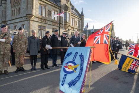 A parade with uniformed individuals and flags, including the Royal Air Forces flag, in front of a historic building.