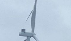 A damaged wind turbine with broken blades stands against a cloudy sky.