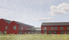 A modern building complex with red exterior, black roofs, and large windows, set in a grassy landscape under a partly cloudy sky.