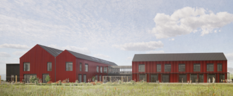 A modern building complex with red exterior, black roofs, and large windows, set in a grassy landscape under a partly cloudy sky.