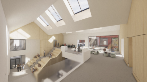 Modern interior with a high ceiling, skylights, and natural wood accents. People are seated on tiered steps and at tables, creating a welcoming, open atmosphere.