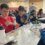 Students sit at tables in a classroom, constructing small structures with straws and clay.