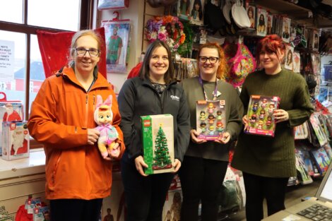 Four people standing in a store holding various boxed toys, with shelves of products in the background.
