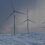 Wind turbines on a snow-covered hill under a cloudy sky.