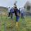 People participating in a tree planting event outside a building. A person in the foreground is digging with a shovel.