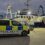 A police van is parked on a dock beside a large, illuminated fishing vessel in the early evening.