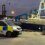 A police van is parked next to a docked fishing vessel named Benarkle III at a harbor in the evening.