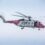 A red and white HM Coastguard helicopter in flight with visible spinning rotors and the side door open.