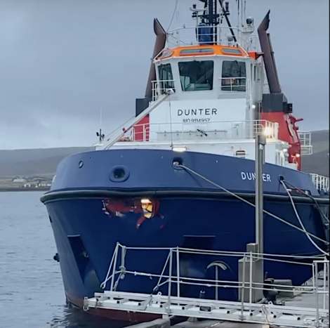 A large blue and white boat named "Dunter" is docked at a pier on a cloudy day.